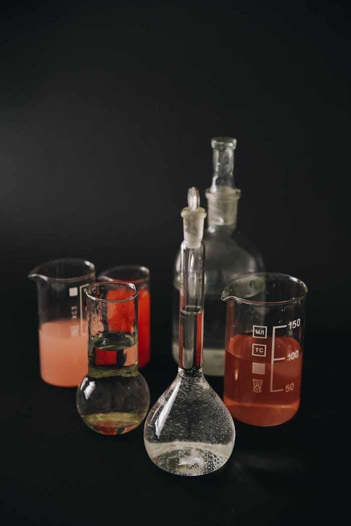 heros-img A collection of laboratory glassware with colored liquids on a dark background.